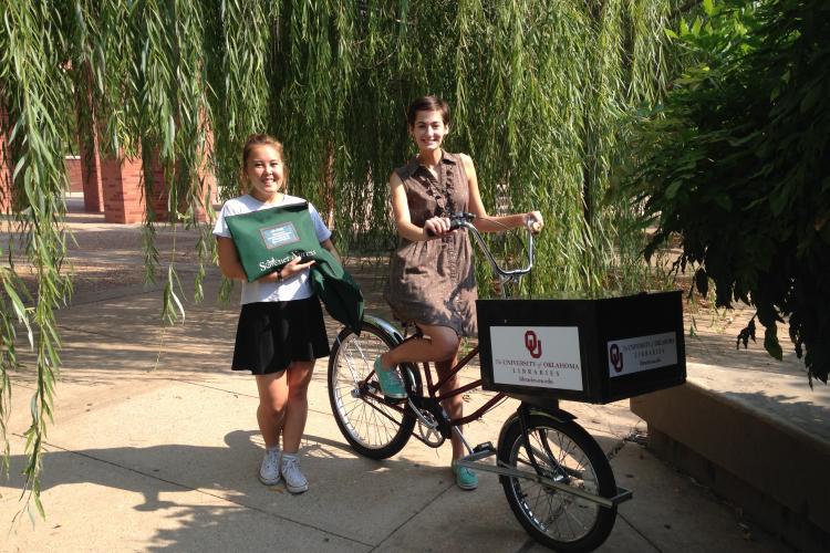 两名妇女和一辆骑自行车，前面有一个送货箱