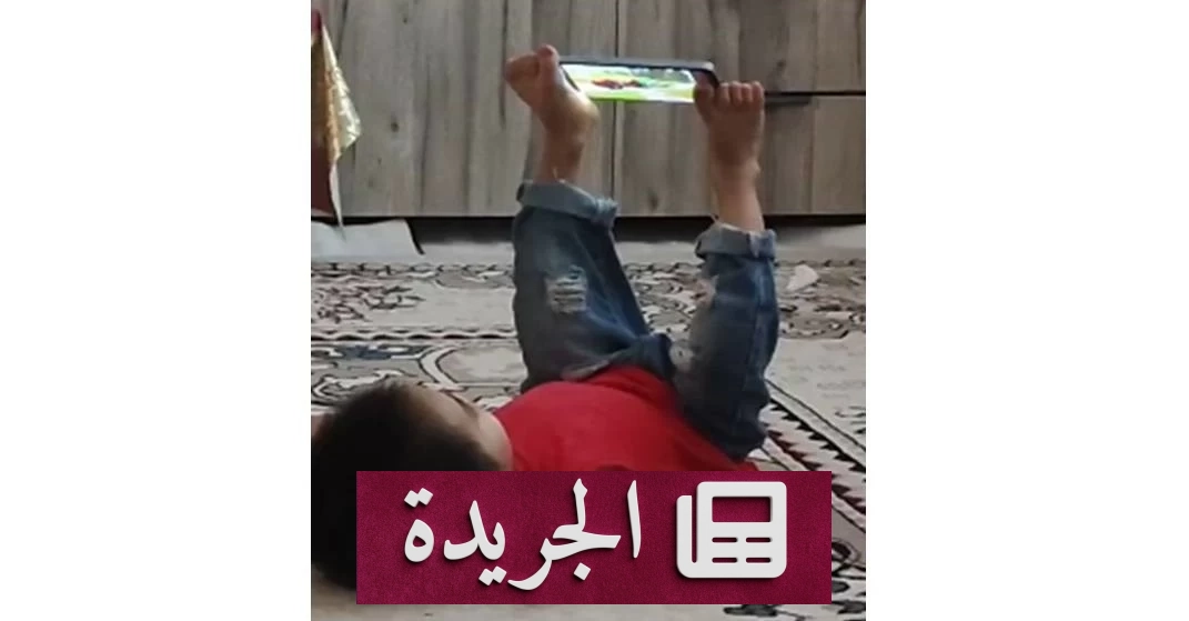 طفل صغير مستلق على الأرض يستخدم قدميه للتحكم بهاتفه الذكي أثناء مشاهدة محتوى